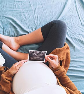 Pregnant woman sitting and holding an ultrasound photo.